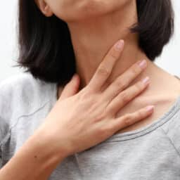 A woman with a sore throat touching her neck.
