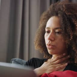 Sick woman putting a hand to her sore throat.