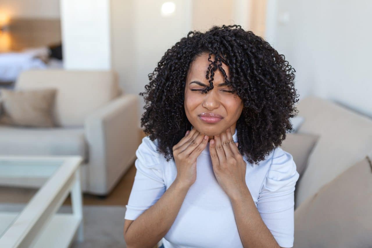 Young woman rubbing her sore throat.