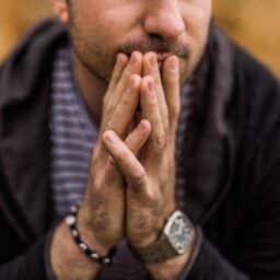 Anxious, stressed man clasping his hands together.