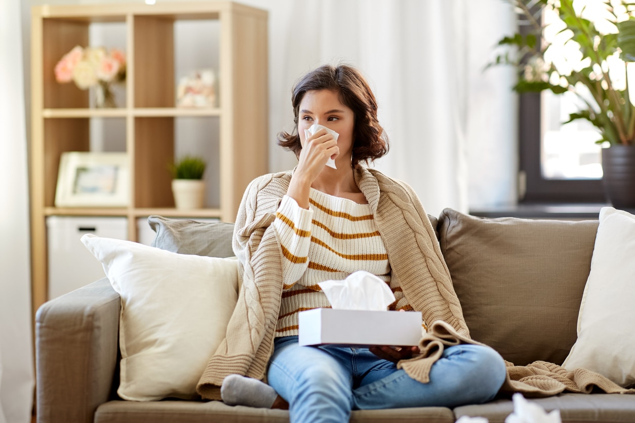 Woman on a couch blowing her nose.